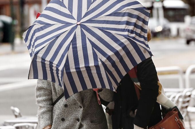 Dos mujeres se protegen con un paragüas de la lluvia y el viento 