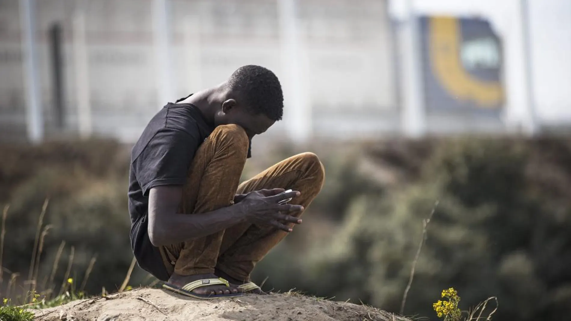 Un inmigrante se sienta de cuclillas en el campamento conocido como "la jungla"junto a la carretera en Calais