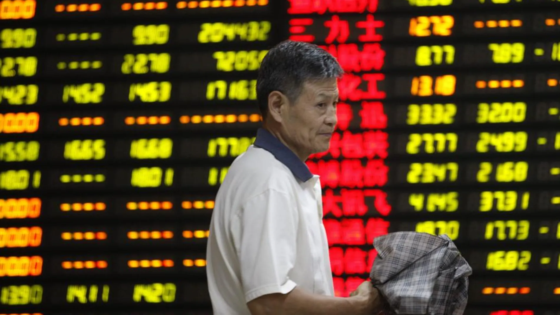 Un inversor pasa delante de una pantalla que muestra la cotización de varios valores en una oficina de corretaje en Huaibei, en la provincia central china de Anhui