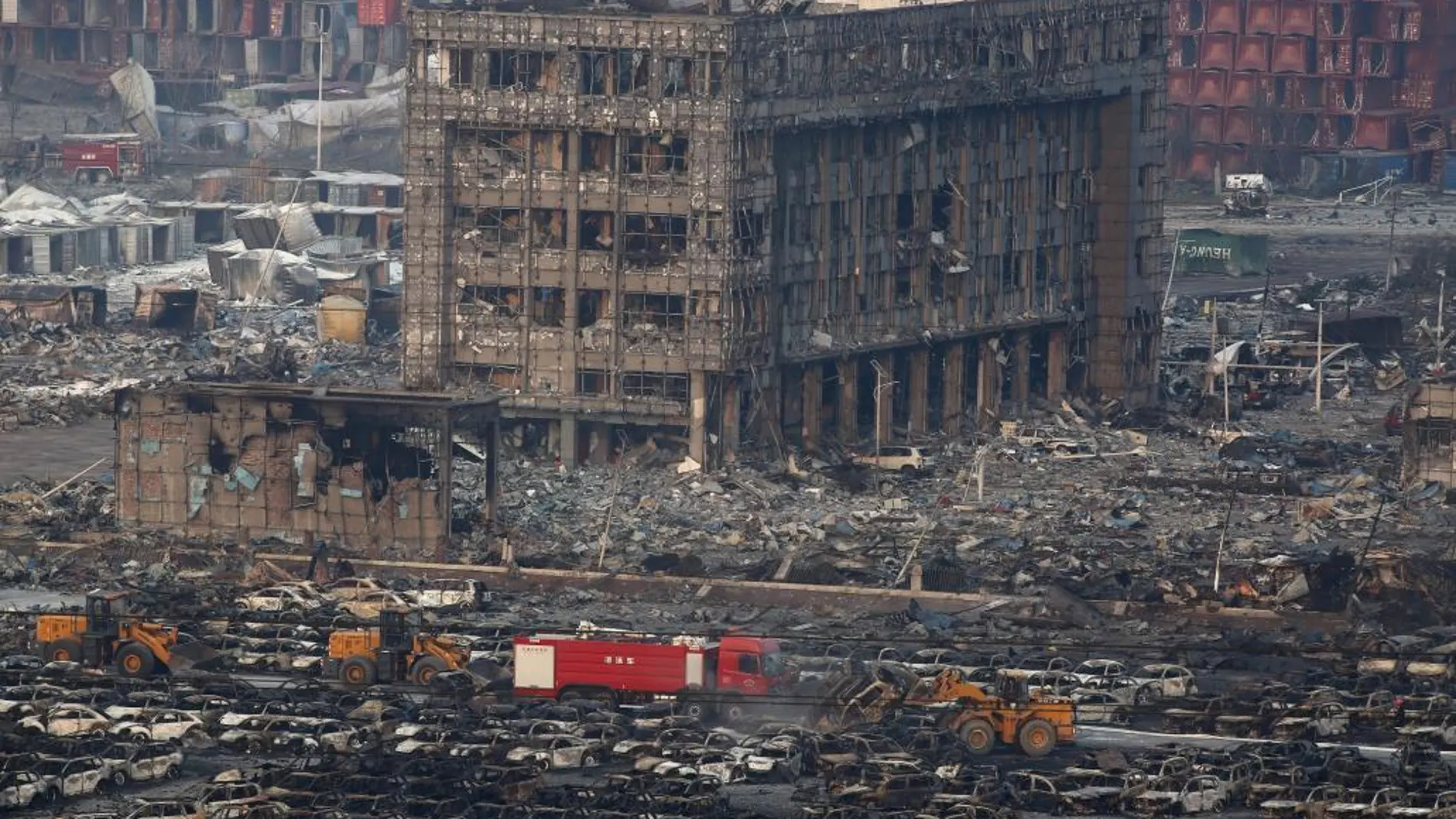 HMiembros de los servicios de rescate trabajan entre cientos de vehículos quemados y varios edificios destruídos tras varias explosiones