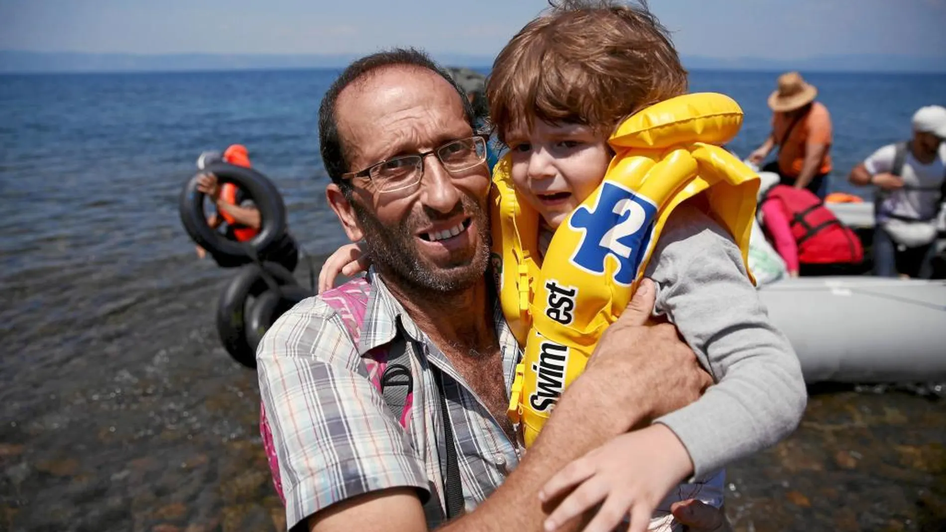 Un refugiado sirio lleva en brazos a un niño tras llegar la isla griega de Lesbos