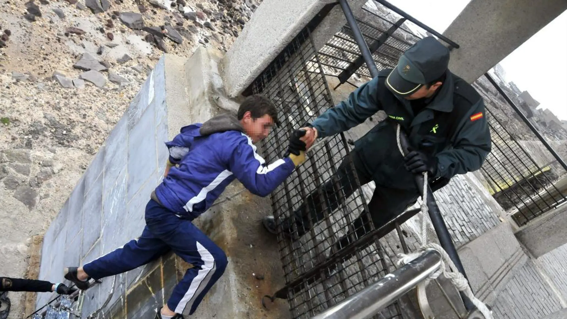 Un guardia civil ayuda a un menor a subir de la escollera en Melilla