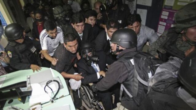 Rafael Correa, con máscra de gas, es evacuado en silla de ruedas del hospital por efectivos del ejército