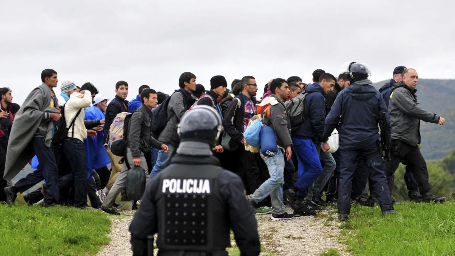 Un agente de policía observa a los refugiados procedentes de Croacia mientras caminan hacia el centro de registro de Brezice, Eslovenia