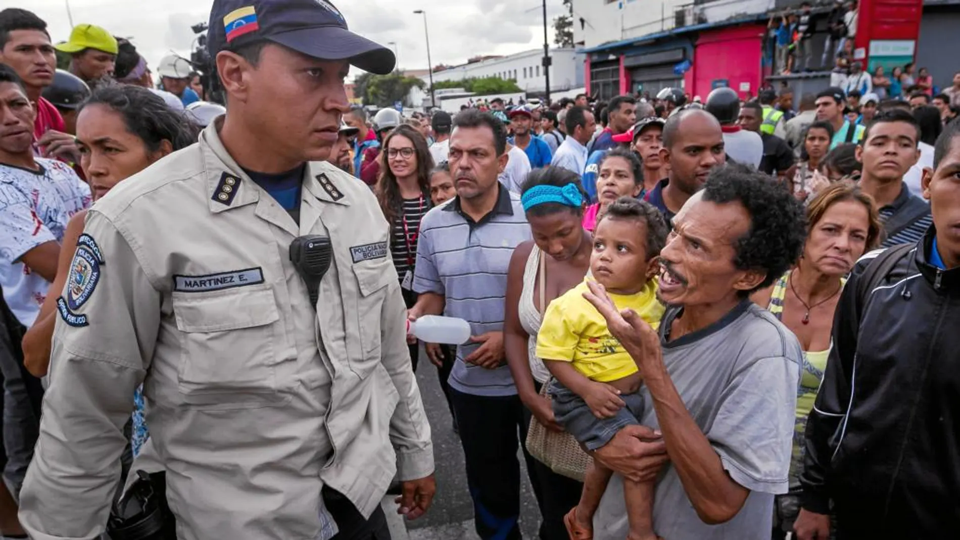 Un hombre con un niño en brazos grita consignas contra un policía en el barrio de Catia, a las afueras de Caracas
