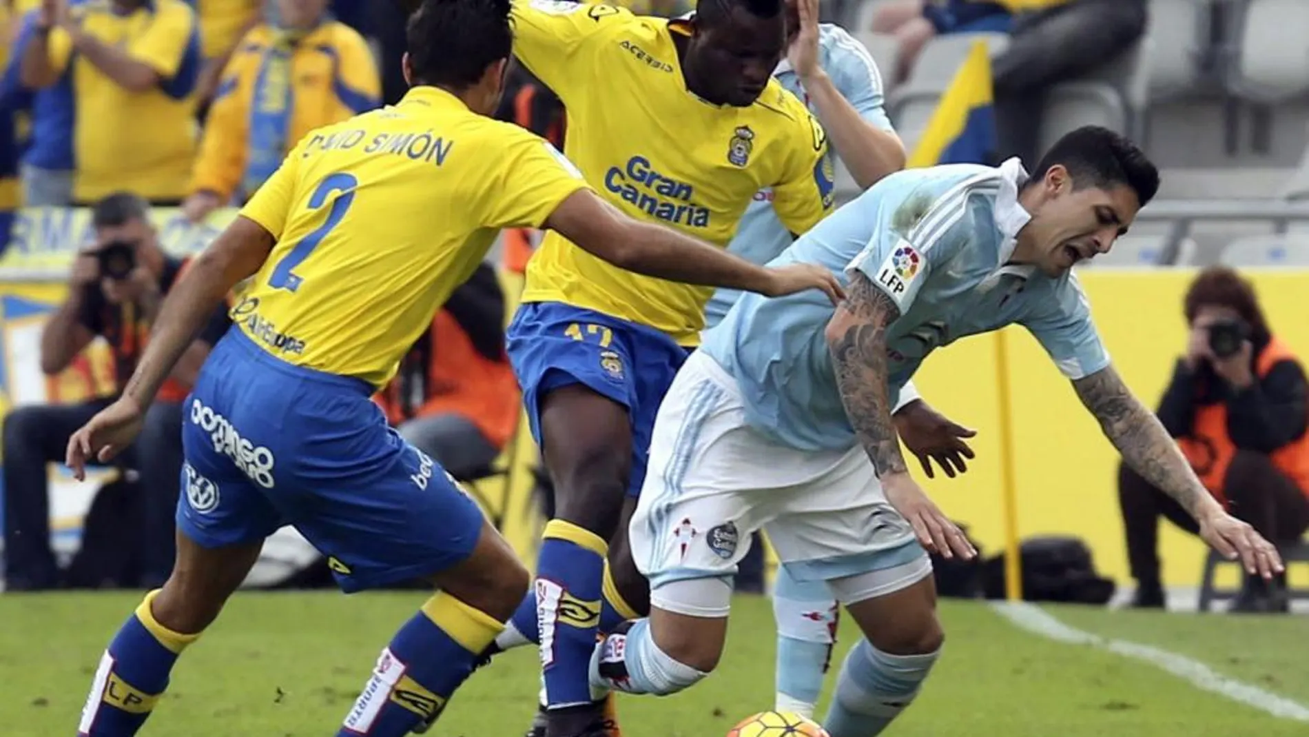 El centrocampista ghanés de la UD Las Palmas, Wakaso Mubarak y su compañero David Simón pelean un balón con el defensa argentino del Celta de Vigo Gustavo Cabral