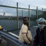Varios inmigrantes esperan saltar una cerca para tomar un tren en su ruta hacia Inglaterra, en Calais (Francia)