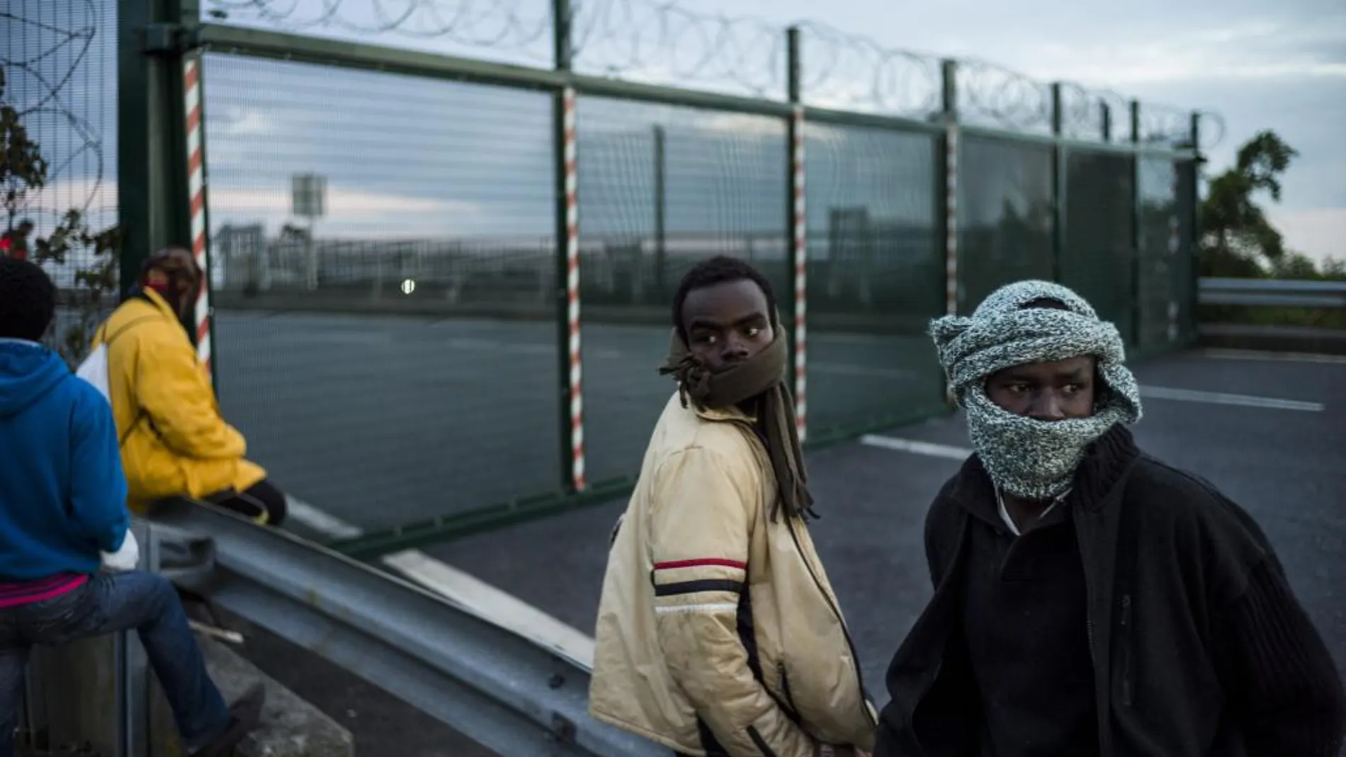 Varios inmigrantes esperan saltar una cerca para tomar un tren en su ruta hacia Inglaterra, en Calais (Francia)