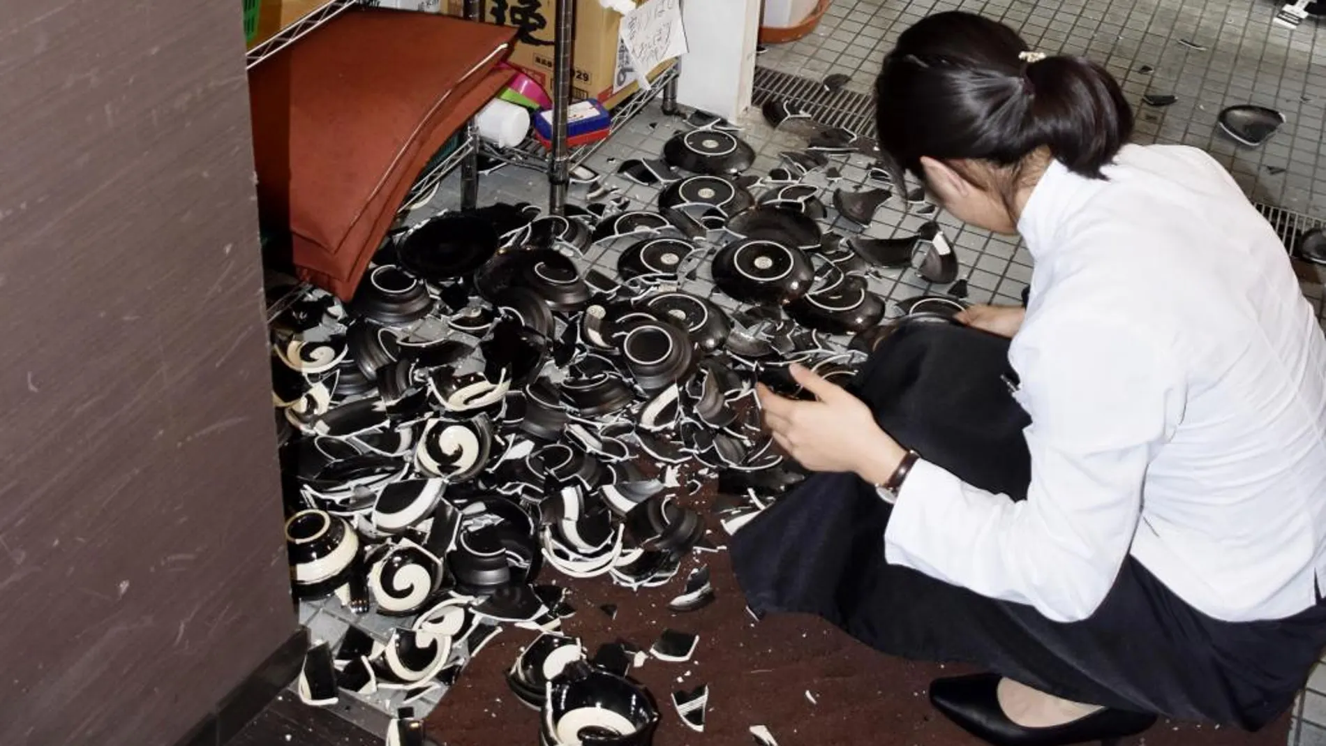 Una mujer recoge vajillas rotas de un restaurante Kumamoto tras el seísmo