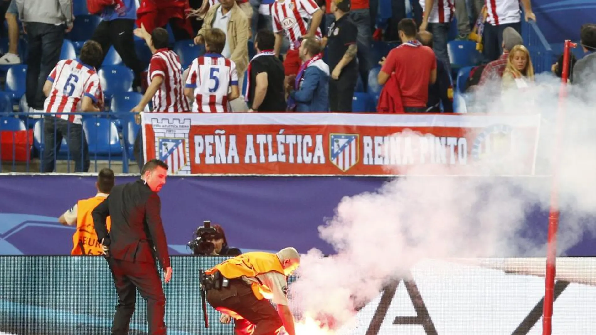 Un operario retira una bengala del terreno de juego durante el partido entre el Atlético de Madrid y el Benfica