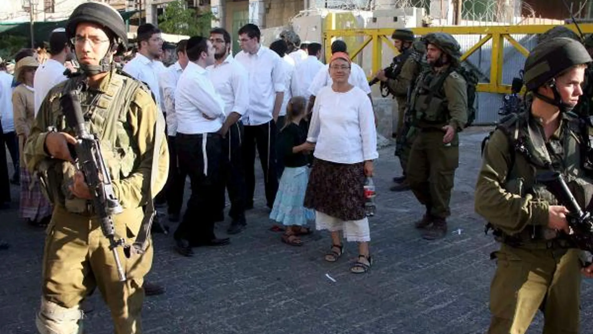 Soldados israelíes bloquean una calle a palestinos que esperan mientras colonos judíos caminan alrededor del mercado palestino en la ciudad cisjordana de Hebrón