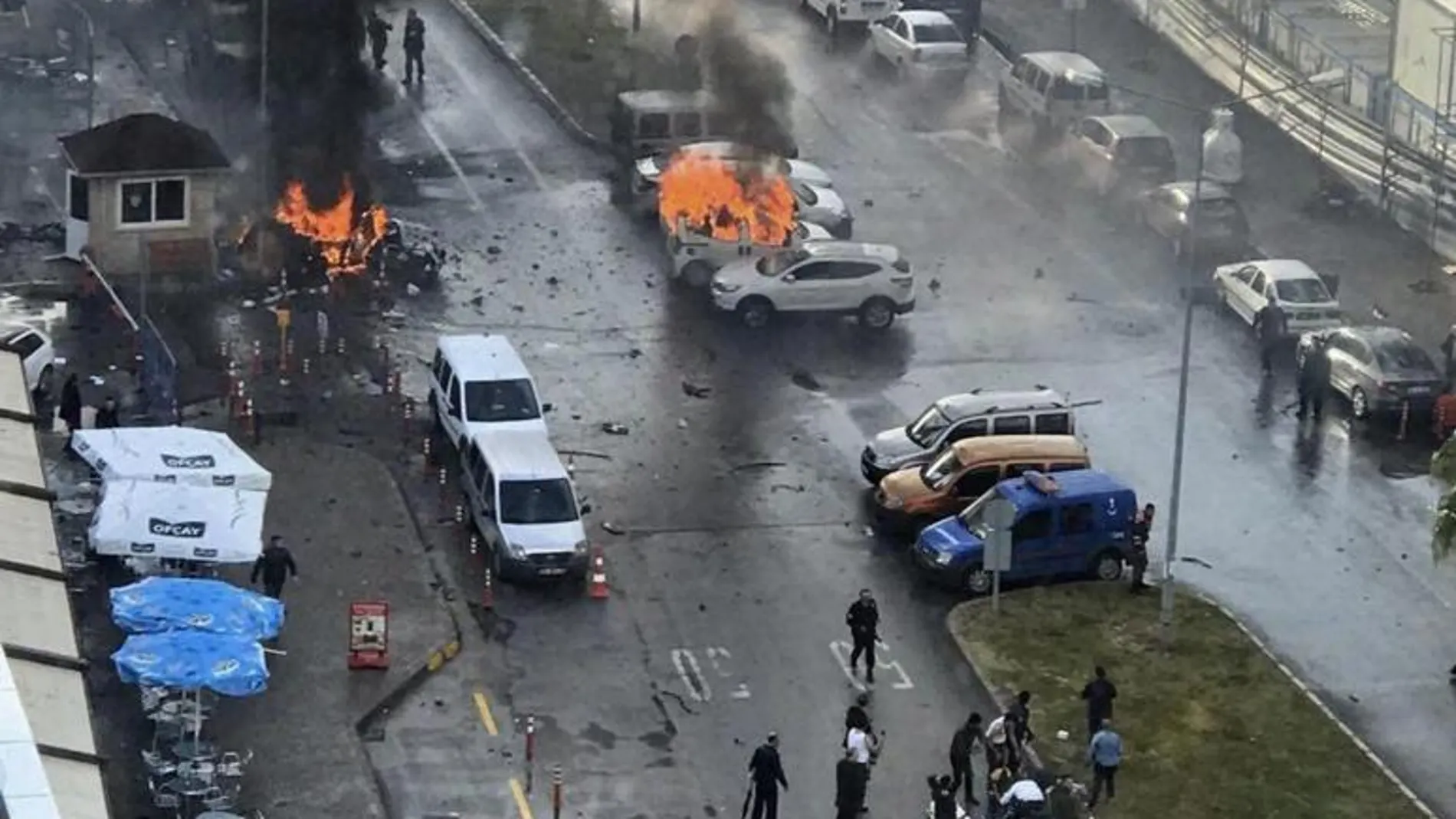 Varios vehículos envueltos en llamas mientras agentes de policía asisten a los heridos después de que explotara un coche bomba frente al Palacio de Justicia de Esmirna