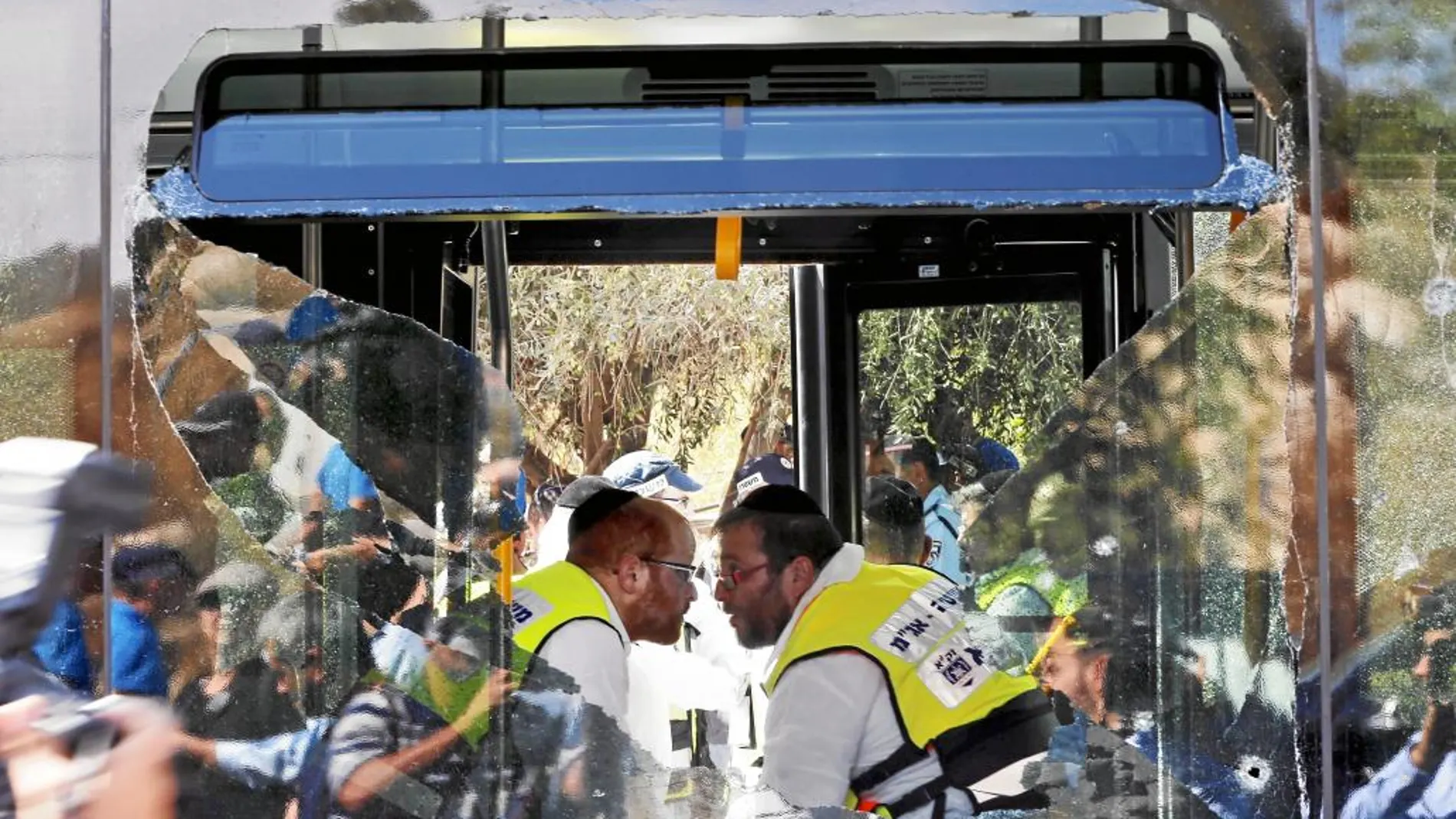 Dos miembros de los equipos de rescate israelí hablan a través del cristal roto de un autobús atacado ayer en Jerusalén