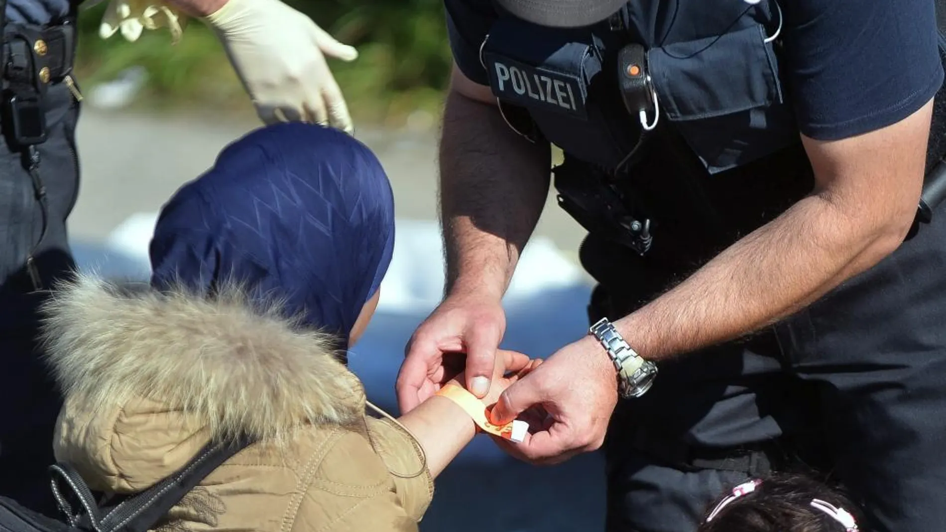 Un policía coloca una pulsera identificativa en el brazo de una mujer a su llegada a Freilassing (Alemania)