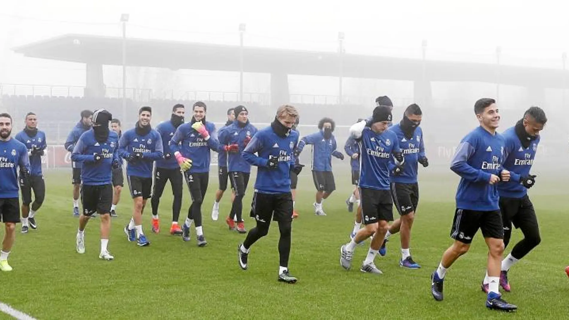 Zidane dando ánimos y la plantilla entrenándose ayer en Valdebebas, entre la niebla de Madrid