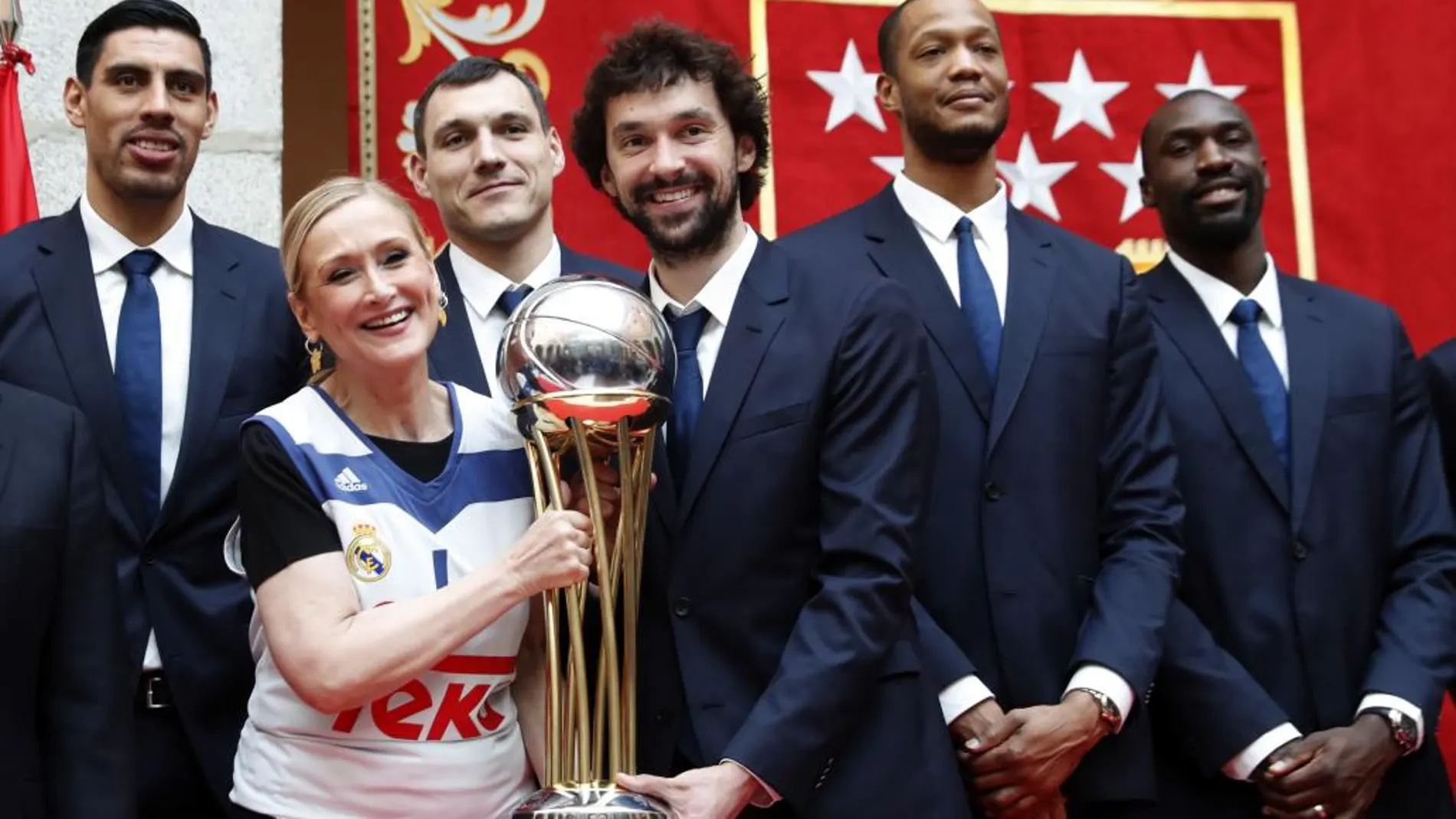La presidenta de la Comunidad de Madrid, Cristina Cifuentes (2i), junto al base Sergio Llull (3d) y los jugadores Ayón, Maciulis, Randolph y Othello Hunter (i-d), posa para la foto de familia con el trofeo durante el homenaje que han recibido los jugadores del Real Madrid de baloncesto en la sede de la Comunidad