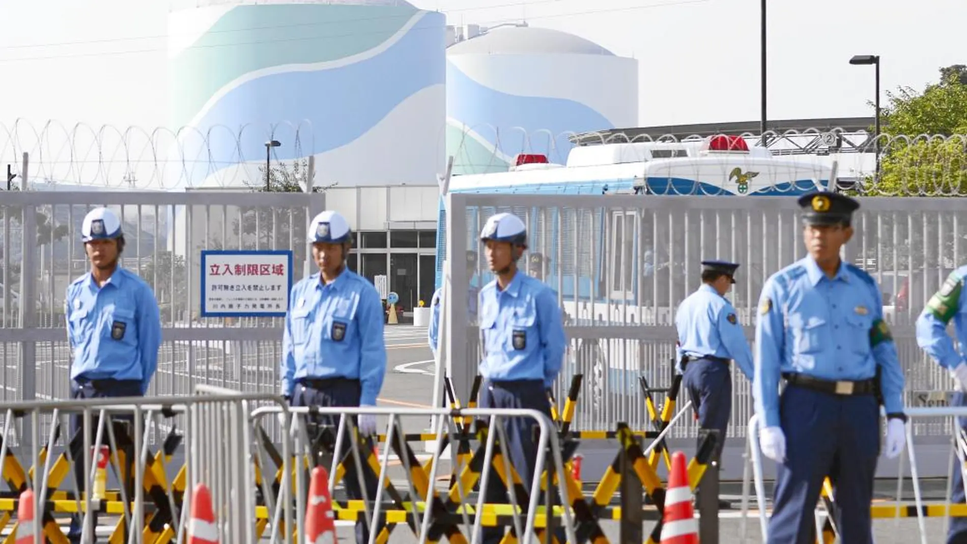 Agentes de policía y guardas de seguridad frente a la verja de entrada de los reactores 2 y 3 de Fukushima