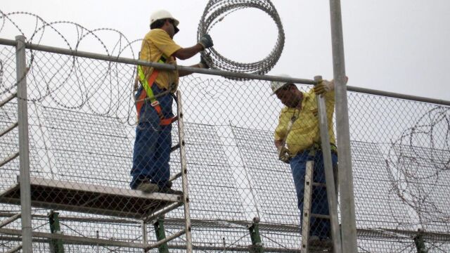 Dos operarios reparando la concertina de la valla que separa España y Marruecos, en Melilla / Efe