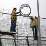Dos operarios reparando la concertina de la valla que separa España y Marruecos, en Melilla / Efe