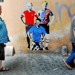 Romanos pasean delante de un mural en la Ciudad Eterna en la que están representados Putin, Trump y Giuseppe Conte