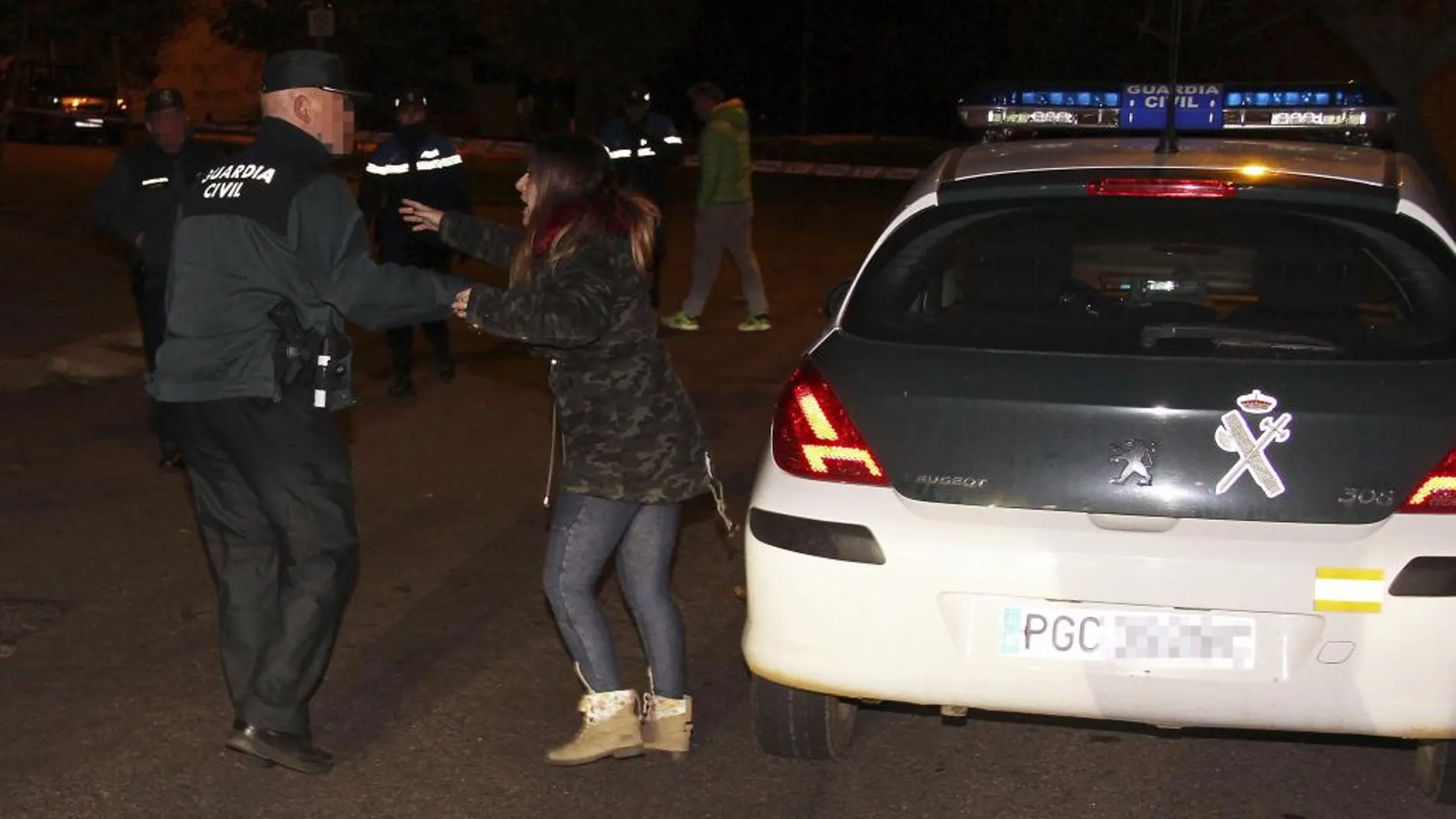 Un guardia civil habla con una mujer cerca de la vivienda donde fueron hallados los cadáveres