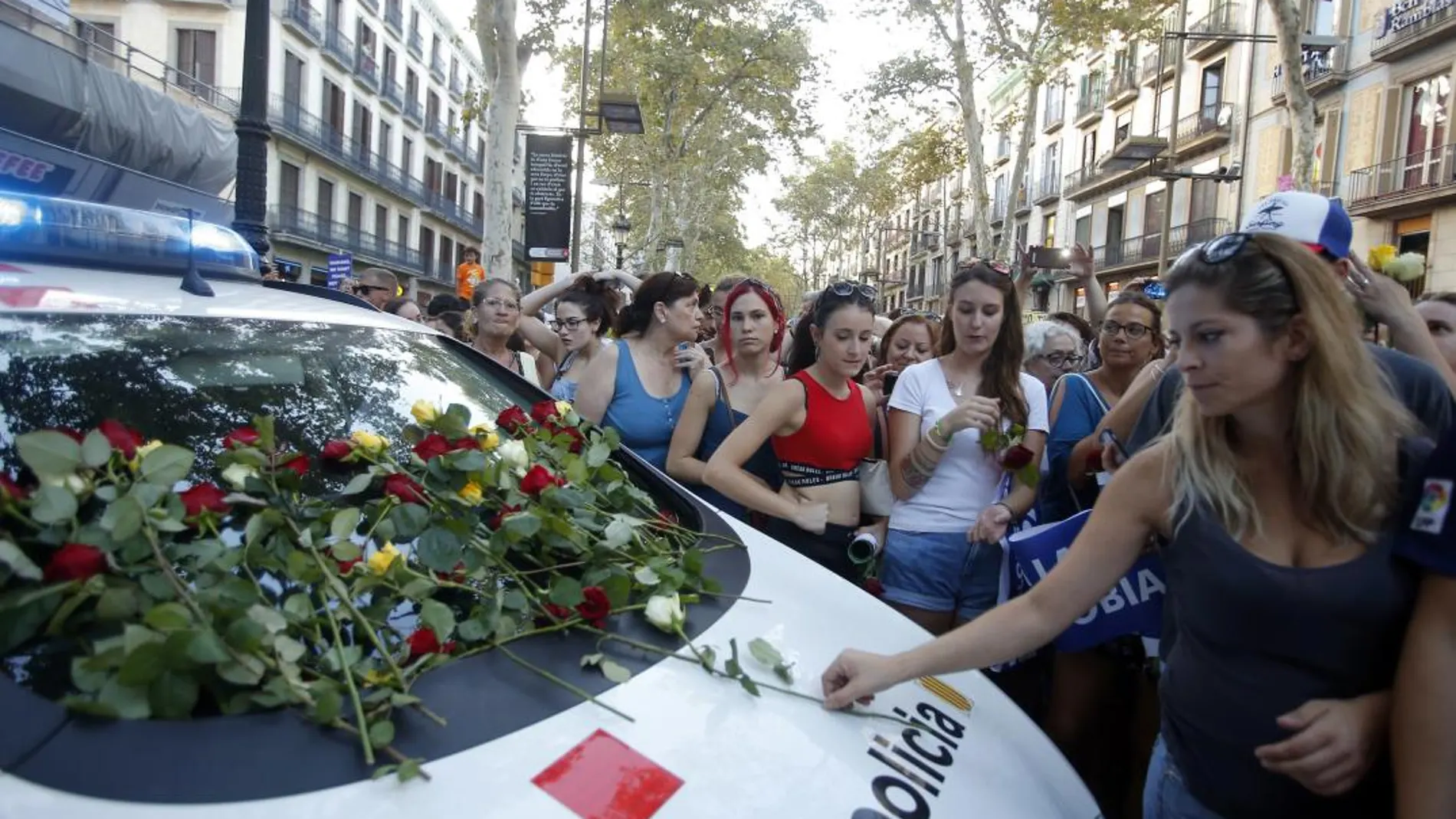 Un grupo de personas depositan rosas en el parabrisas de un coche policial tras los atentados de Barcelona