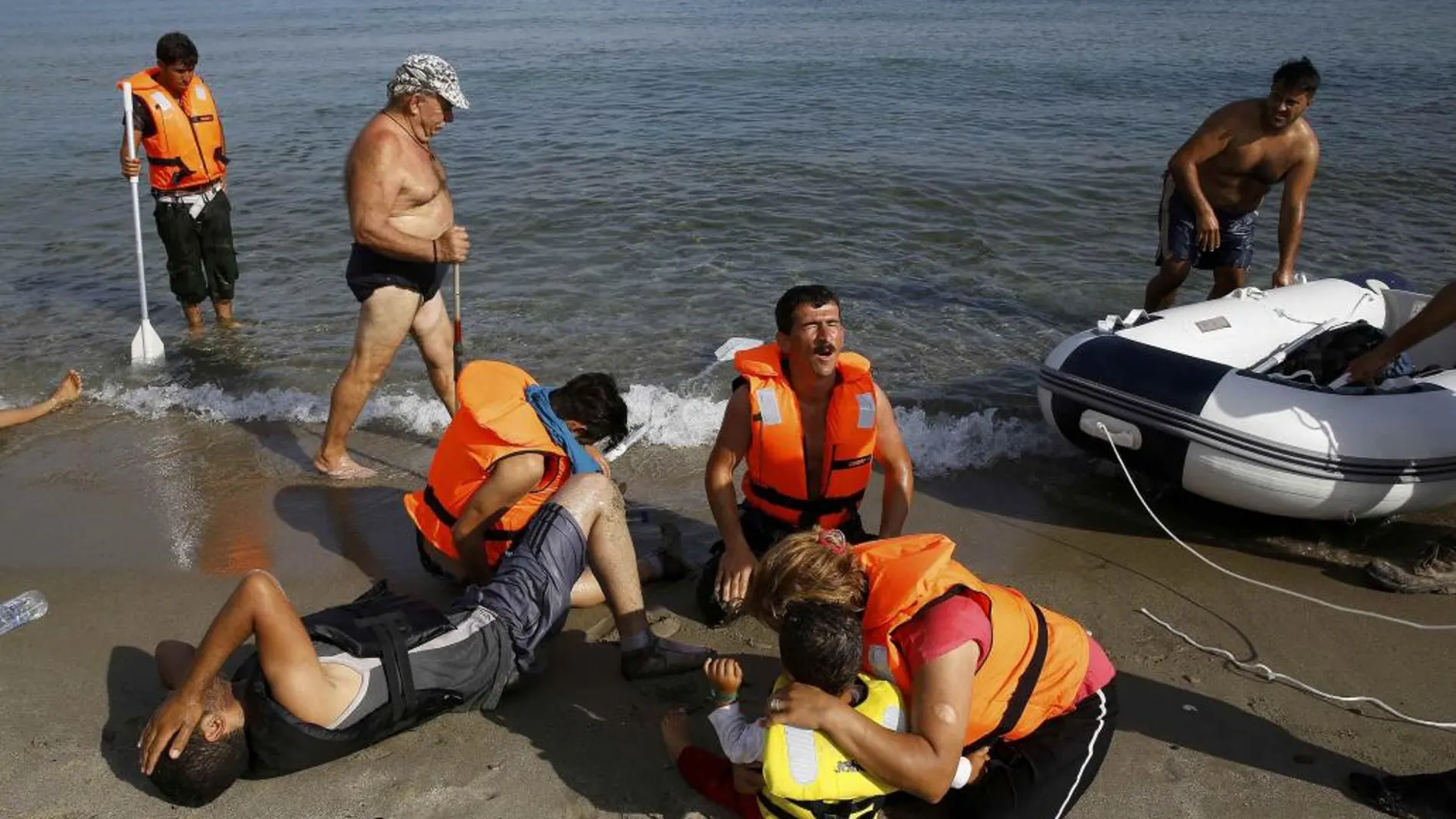 Un turista pasa junto a una familia iraní que acaba de llegar en un bote a la isla griega de Kos