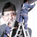 Dos operarios colocan el cartel de Rajoy en la sede del PP de Madrid