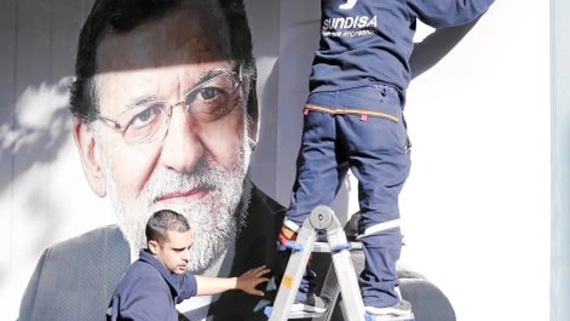 Dos operarios colocan el cartel de Rajoy en la sede del PP de Madrid