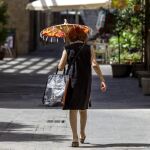 Una mujer camina por una calle del barrio del Carmen de Valencia protegiéndose del intenso sol con una sombrilla.