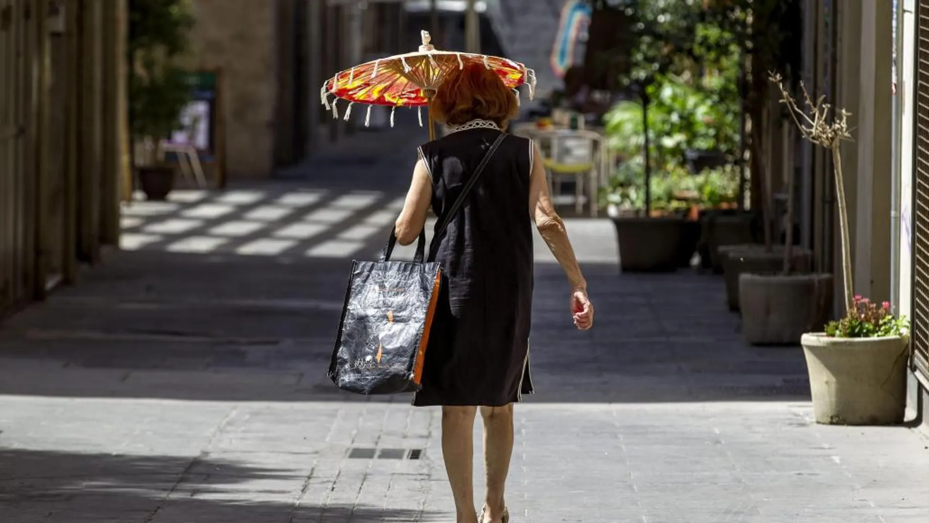 Una mujer camina por una calle del barrio del Carmen de Valencia protegiéndose del intenso sol con una sombrilla.