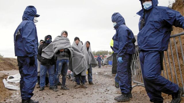 Varios inmigrantes esperan las órdenes de los guardias croatas tras su llegada al campamento de Opatovac