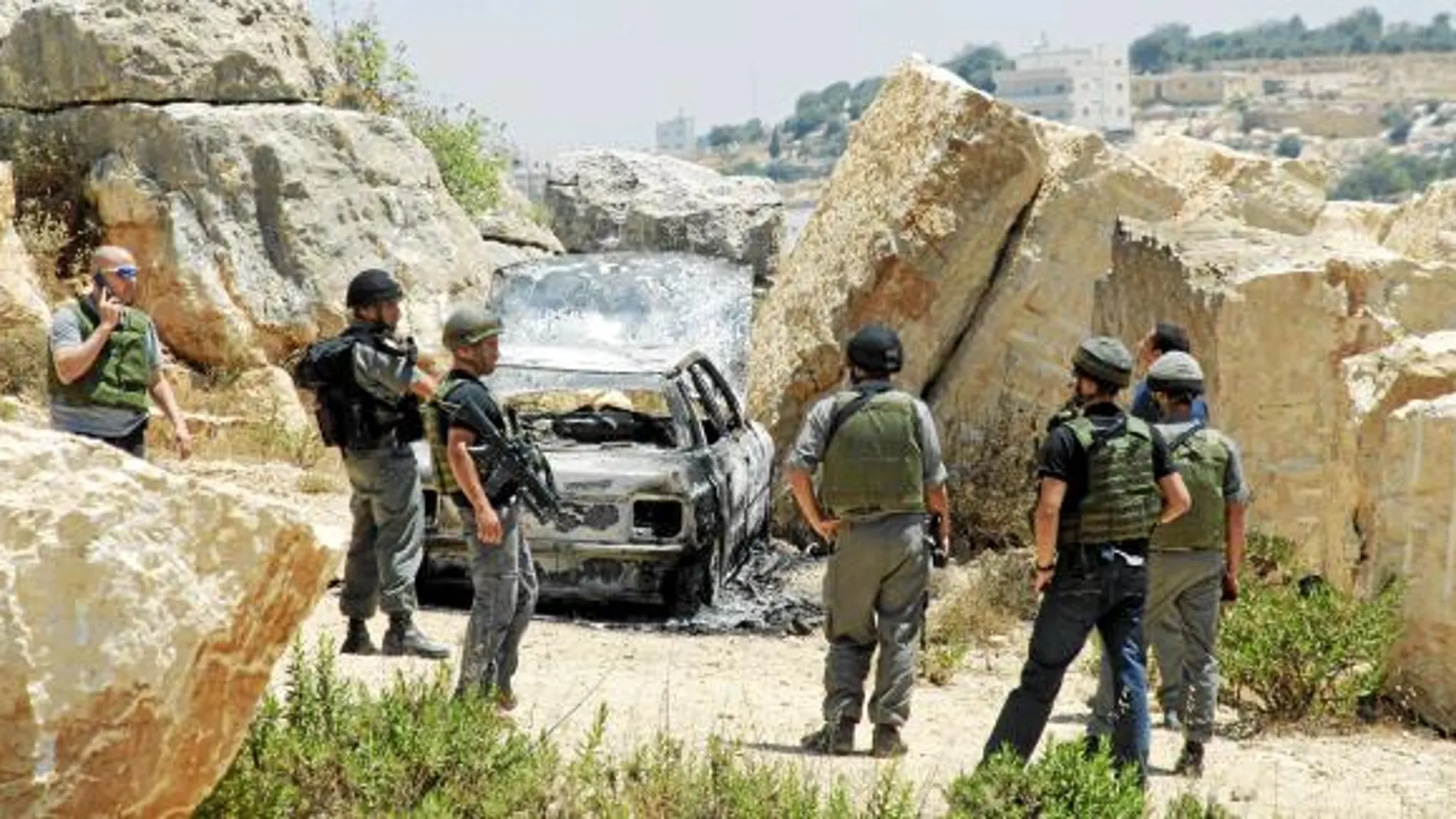 Soldados israelíes inspeccionan un automóvil calcinado en el lugar donde fue emboscada una patrulla policial, cerca de la ciudad cisjordana de Hebrón