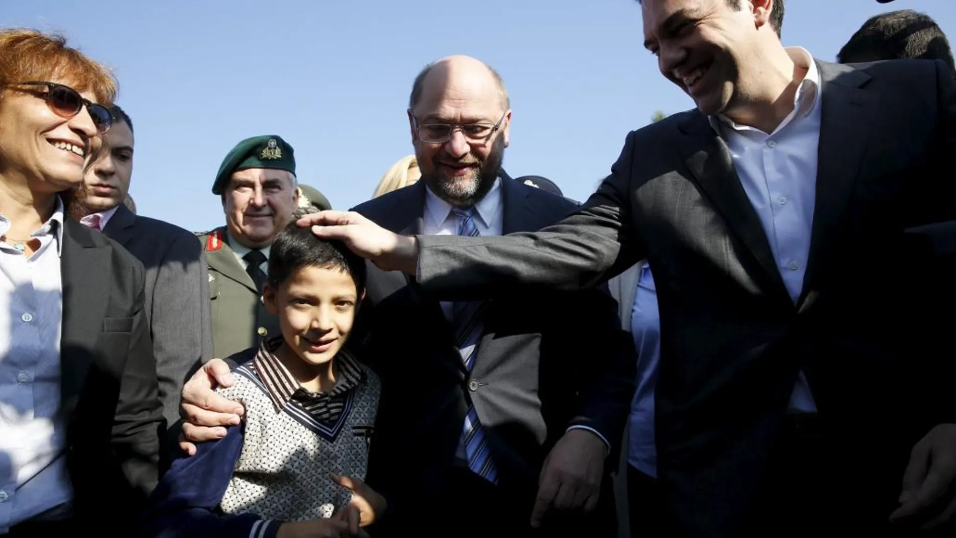 El primer ministro griego, Alexis Tsipras, y el presidente del Parlamento Europeo, Martin Schulz saludan a un niño refugiado.