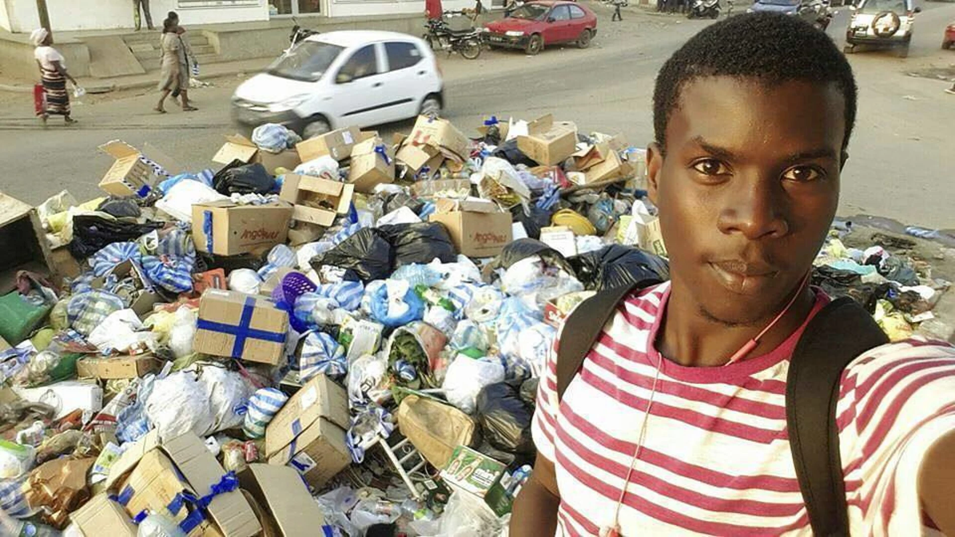 Un joven posa delante de un montón de basura acumulada en una calle de Luanda