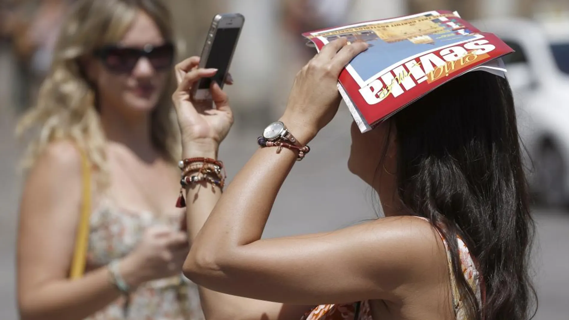 Una turista se fotografía mientras se proteje del sol con una guía turística de Sevilla