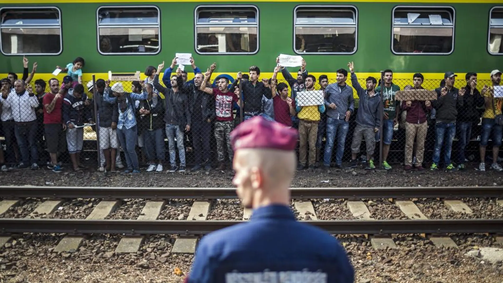 Un policía vigila mientras refugiados piden poder continuar su viaje rumbo a Europa Occidental.