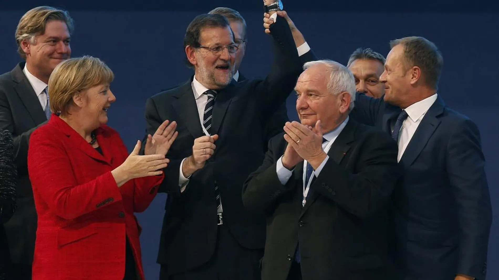 Donald Tusk (d), levanta el brazo de Rajoy (c), junto al presidente el PPE, Joseph Daul (2d), y Angela Merkel (i), mientras posan para la foto de familia del Congreso del Partido Popular Europeo (PPE).