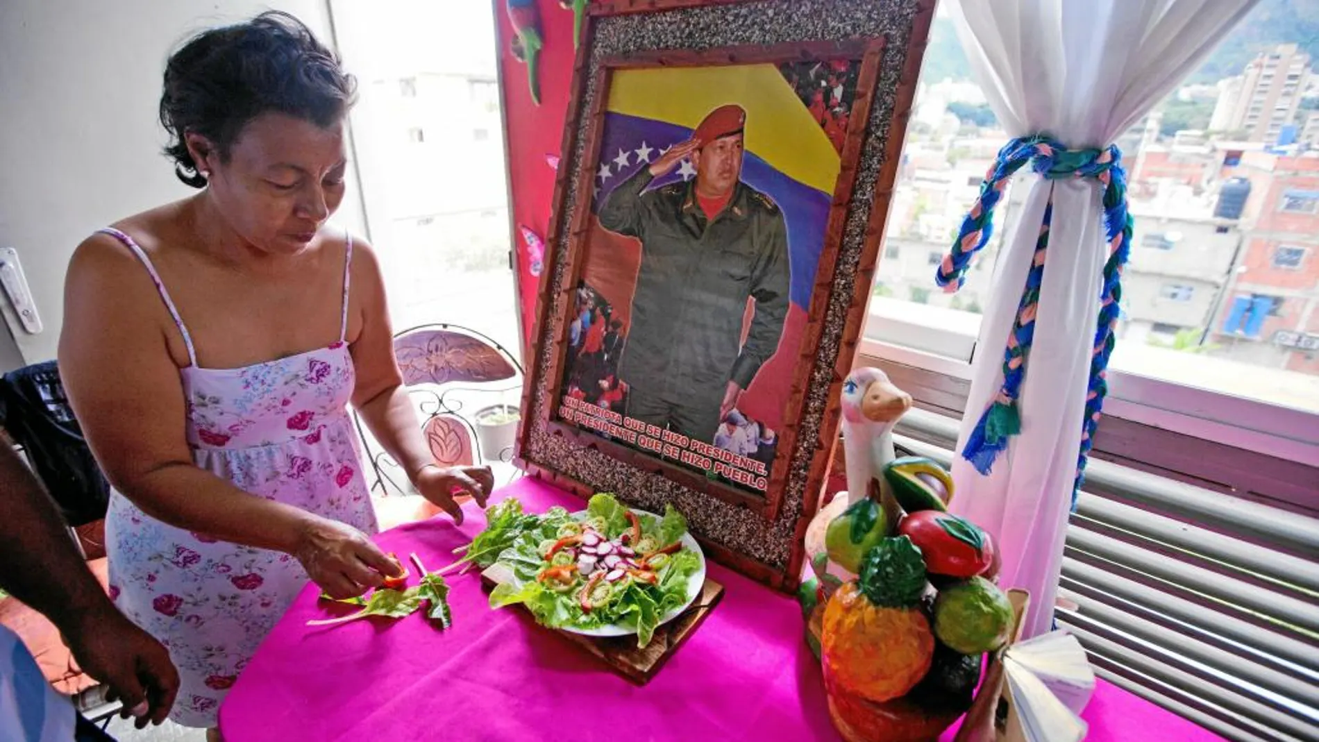 Una mujer venezolana ultima prepara la comida con una imagen de Hugo Chávez presidiendo el salón de su casa en Caracas