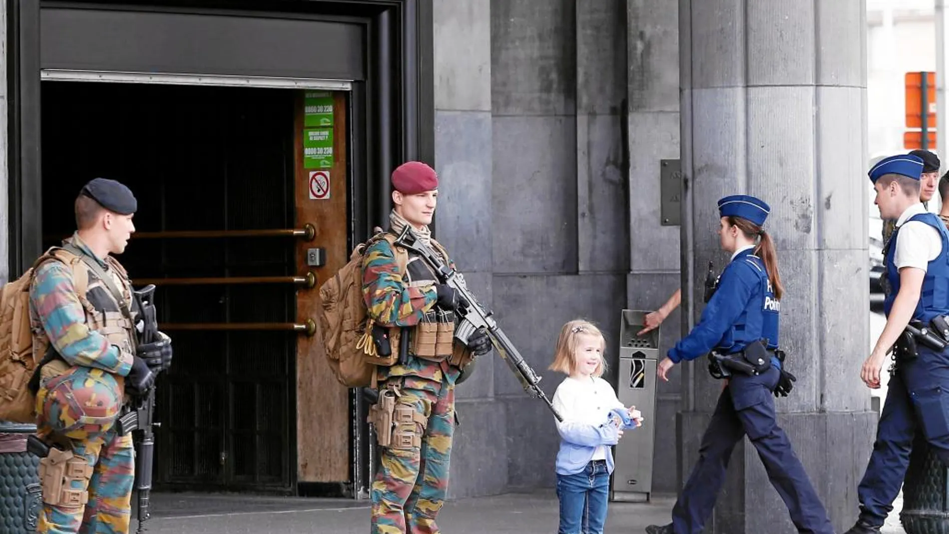 Una niña se deja fotografiar por un familiar junto a dos soldados que vigilan la entrada de una estación belga