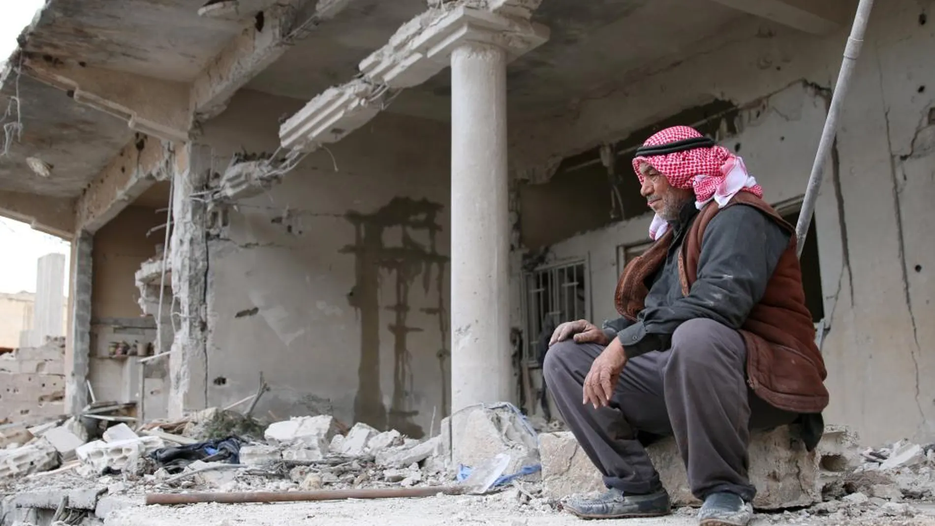 Un hombre descansa cerca de una casa dañada por los bombardeos en Deraa