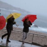 Tres mujeres se protegen de la lluvia en el paseo marítimo de A Coruña.