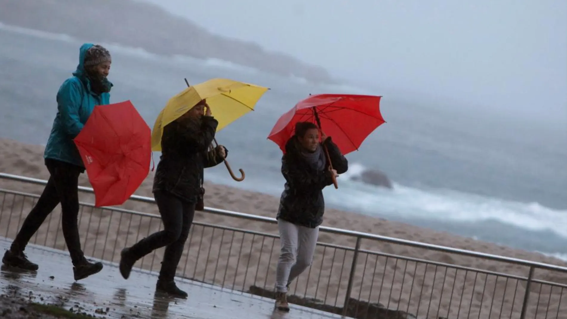 Tres mujeres se protegen de la lluvia en el paseo marítimo de A Coruña.