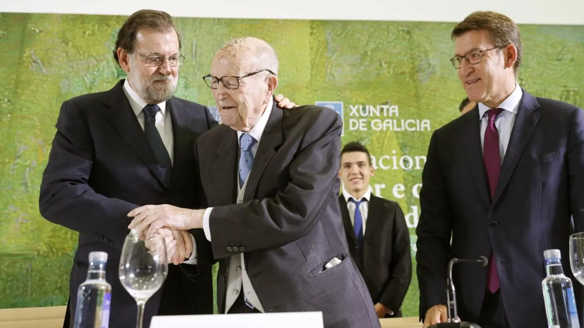 El jefe del Ejecutivo, Mariano Rajoy (i), abraza al primer presidente electo de la Xunta de Galicia, Xerardo Fernández Albor (c), antes de imponerle la Medalla de Oro al Mérito en el Trabajo, junto al presidente de la Xunta, Alberto Núñez Feijóo
