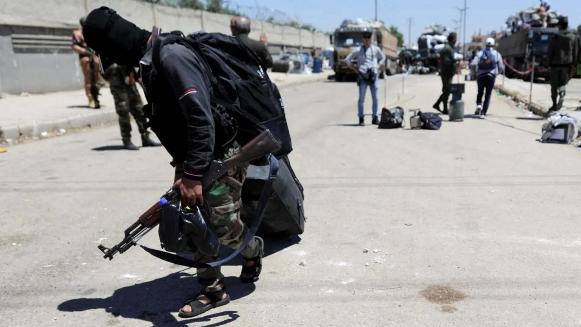 Un combatiente rebelde lleva su maleta y sus armas hacia el autobús para evacuar Homs