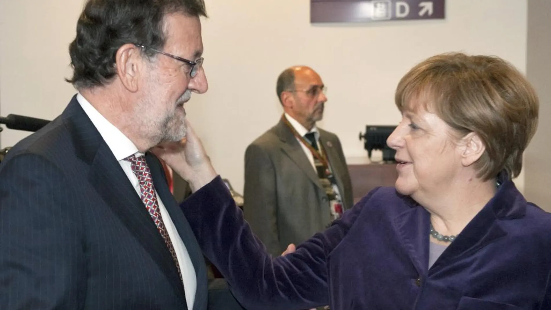 La canciller alemana Angela Merkel toca a Mariano Rajoy en la cara, donde recibió el puñetazo.
