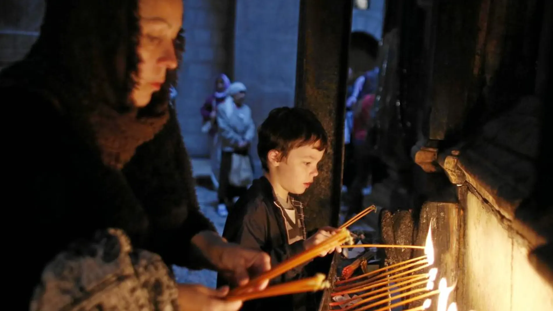 Una mujer y un niño encienden una vela en la basílica del Santo Sepulcro de Jerusalén