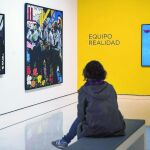 Una mujer observa sentada diferentes cuadros de la exposición temporal "Reflejos del Pop"