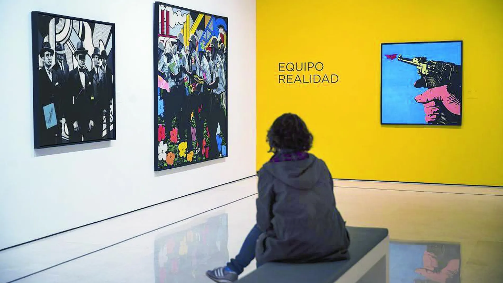 Una mujer observa sentada diferentes cuadros de la exposición temporal "Reflejos del Pop"