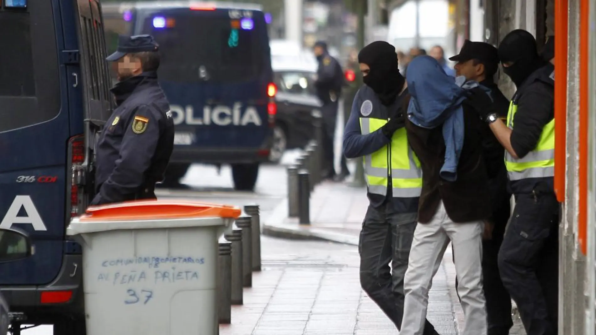 Dos efectivos de la Policía acompañan a uno de los detenidos en el madrileño barrio de Vallecas por formar parte de un grupo vinculado al Estado Islámico